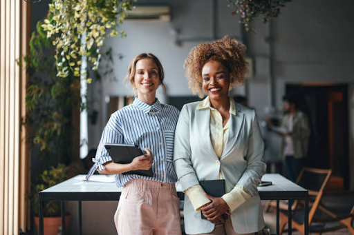 Two businesswomen smiling, representing diverse entrepreneurs, in an office setting discussing free zone licenses.