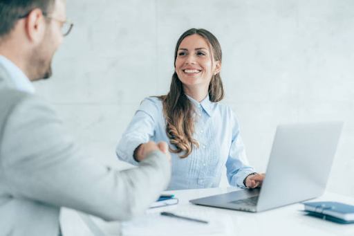 Business professionals shaking hands and smiling over a laptop, discussing UAE free zone license costs.